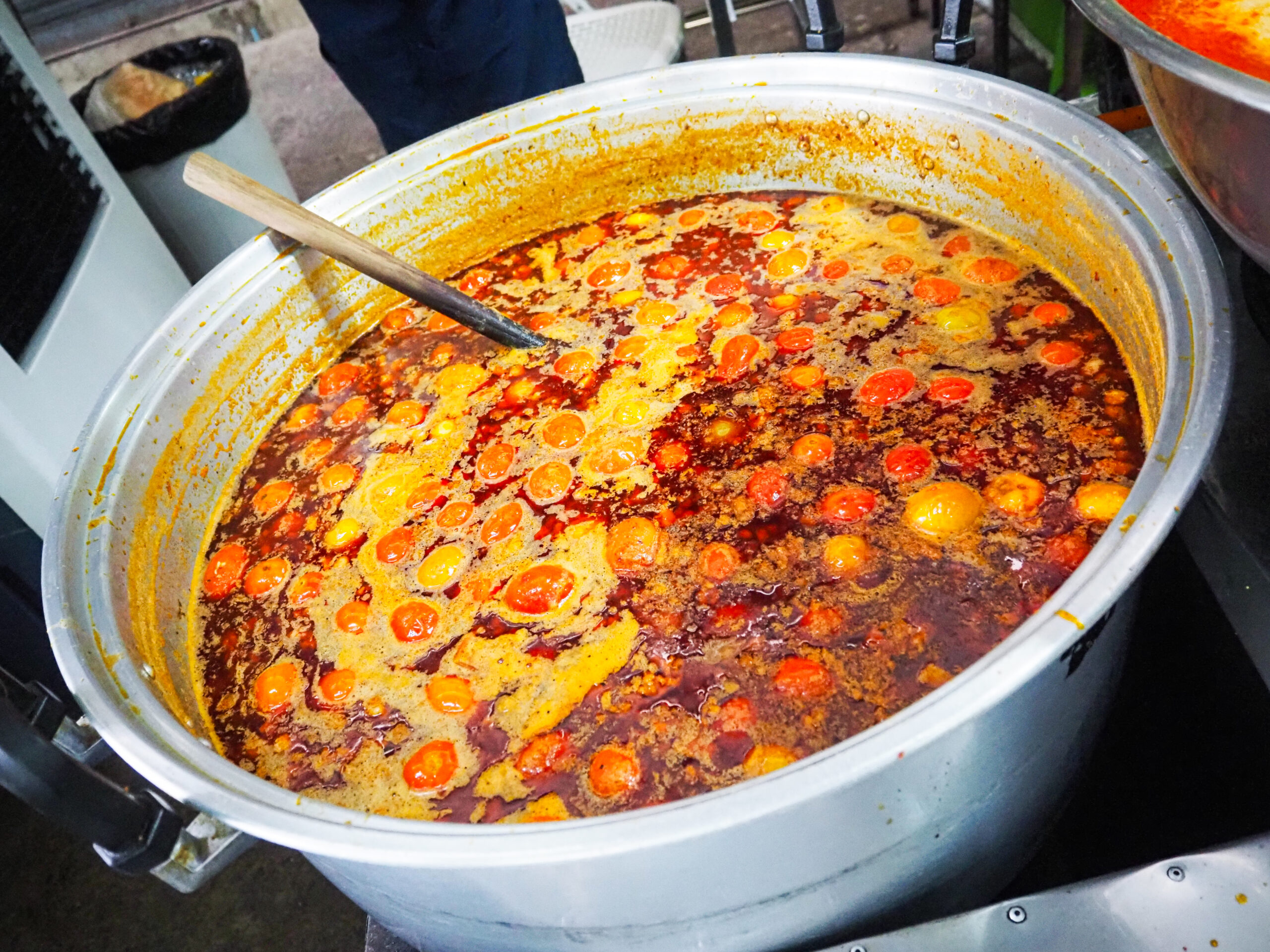 チェンマイのローカル市場にあるカノムジーンサンパコーイのナムギャオ トマトと豚骨の激辛スープ麺　大鍋で煮込まれるナムギャオ 赤いトマトが浮かぶスープ